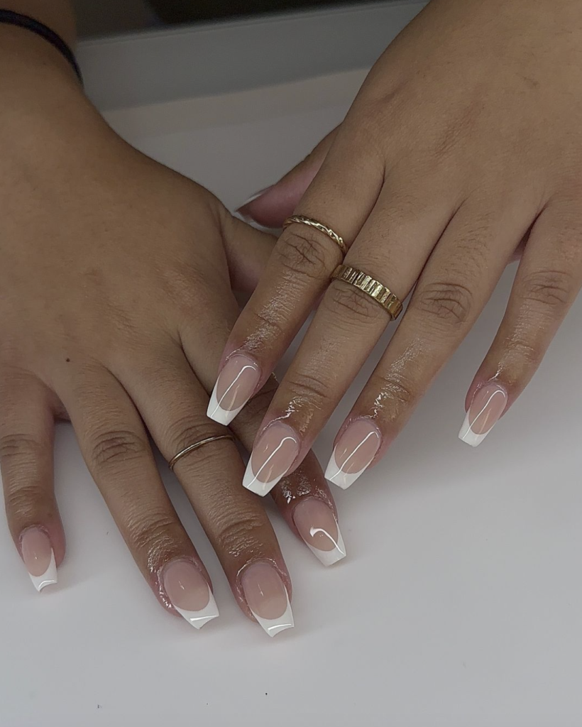Hands showing a classic French manicure with white tips on a nude base.